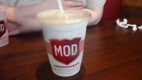 A white and red MOD Pizza plastic cup on a brown wooden table.