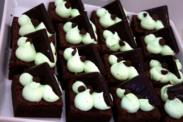 A black Brownie, with white cream, on a grey background.
