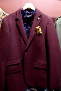 A brown blazer, with a gold Deer pin, on a gold coat hanger.